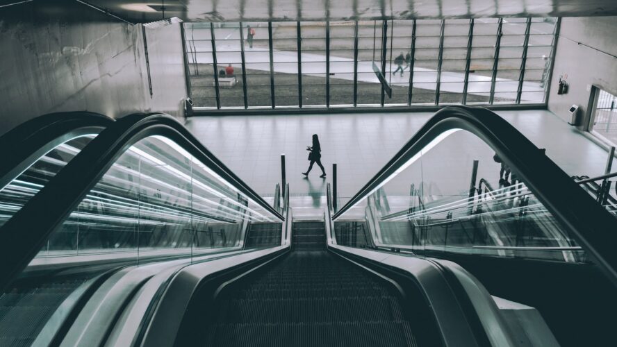 grayscale photography of person walking near escalator