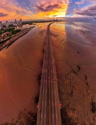 aerial view of a multiple lane highway stretching along a sandy coastline at sunset