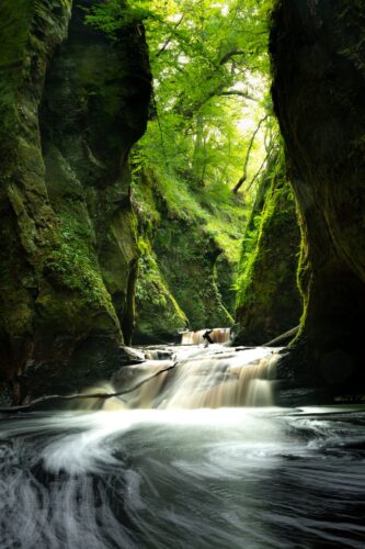 time lapse photo of river between mossy rocks